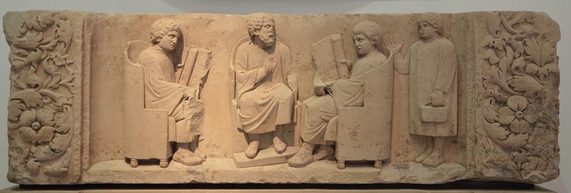 Relief found in Neumagen near Trier, a teacher with two discipuli and a puer capsarius (180-185 CE).