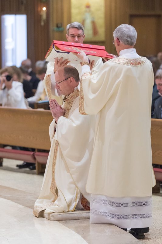 Rite of Episcopal Ordination by Shawn McKnight, Jefferson City, 2018. The depicted persons are not  related to the abuse scandal. However, I thought, that the depicted scenery – Two church authorities cover the bishop-to-be with a large book, probably a Bible –  perfectly symbolizes the systematic cover-up of pedo-criminal figures in the Church.